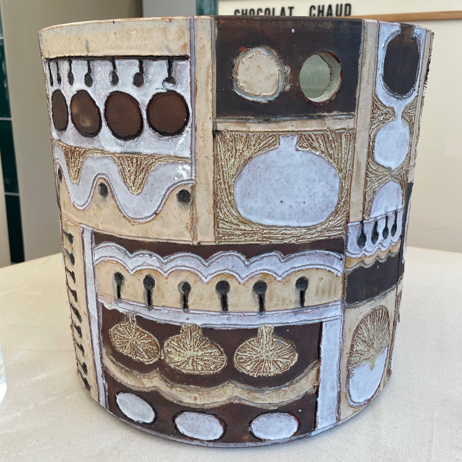 Imposant vase de forme cylindrique orné d’un patchwork de petits tableaux de composition brutaliste, en faïence brute à texture rugueuse avec des motifs émaillés contrastés, dans des tons bruns, blancs et ocre, circa 1970 (fin des années 1960 - avant 1972), signé sous la base "Perignem". On connaît ce type de décoration sur des objets généralement plus petits et traité le plus souvent en frise. Diamètre 36 x 33,5 cm de hauteur., Elisabeth Vandeweghe (1946).